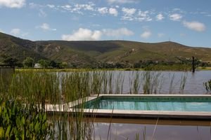 A serene countryside view with a swimming pool and green hills under a blue sky.